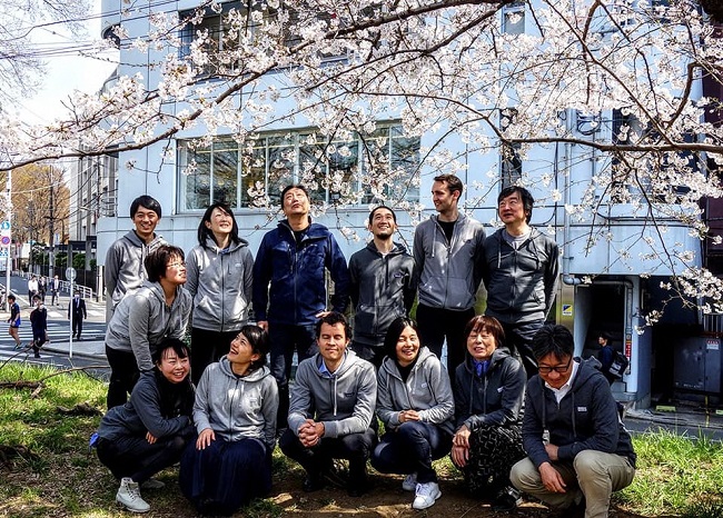 ▲東京本社前の桜並木前での１枚。多様なスタッフがいて、日々活発なコミュニケーションをとっている
